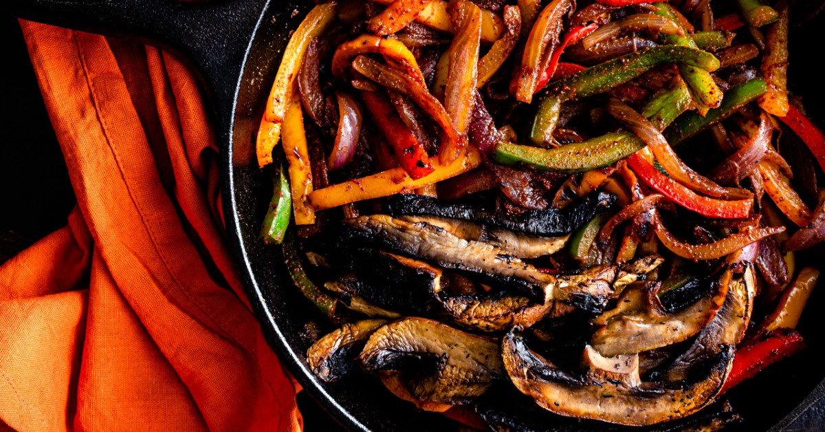 Portobello mushrooms, red and green bell peppers and onions sliced for fajitas and cooking in a pan.