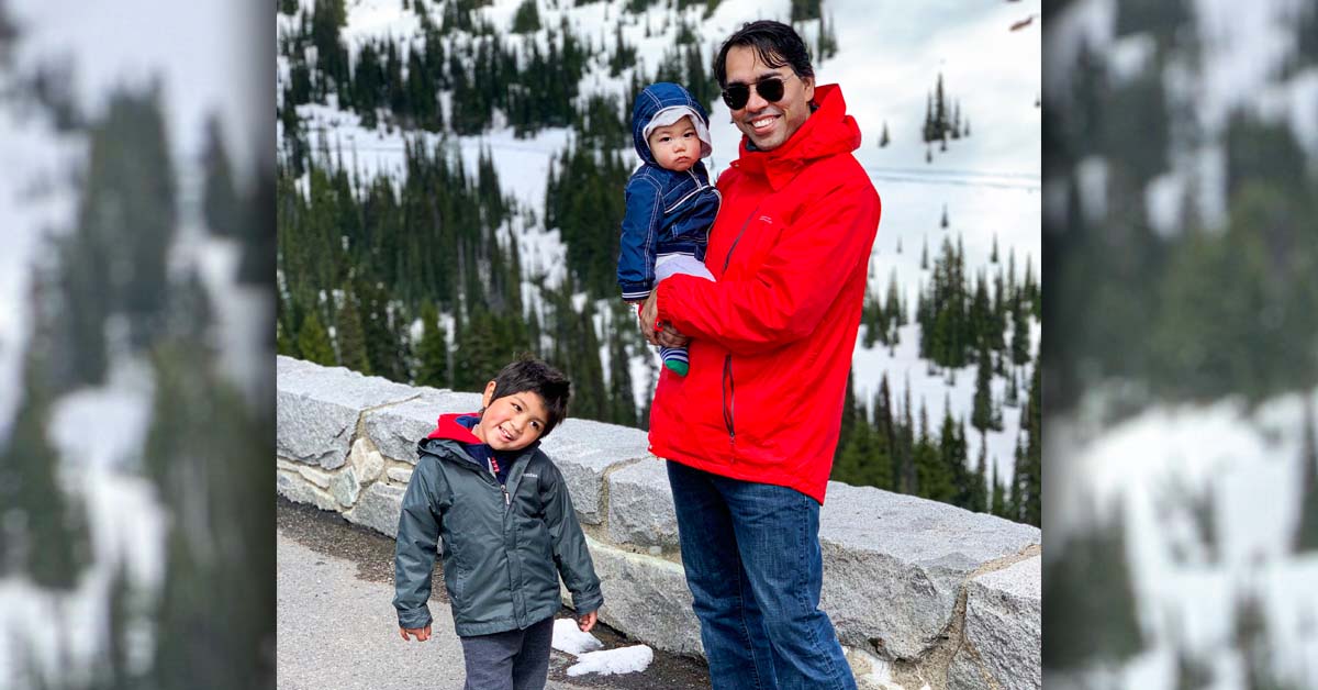 Dr. Prabhpreet Singh of Aurora BayCare Cardiology poses with his children before a snowy, mountain landscape.